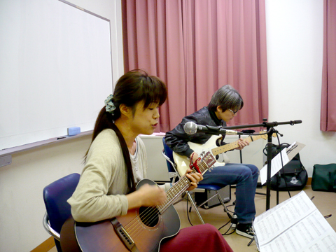 40代女性の生徒さんのギターの弾き語りと伴奏する講師の様子