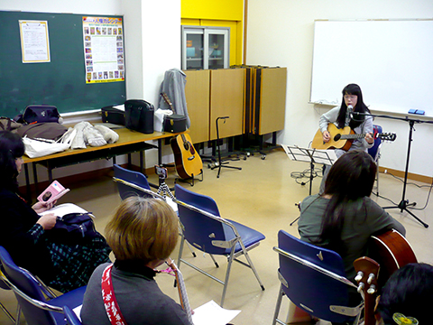 40代女性の生徒さんのギターの弾き語りとそれを聴く生徒さんたちの様子