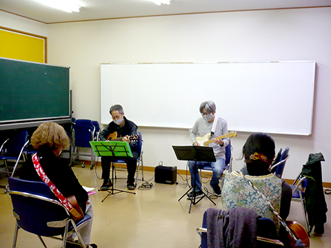 60代男性の生徒さんと講師のギター演奏とそれを聴く生徒さんたちの様子
