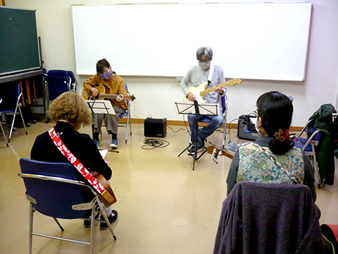50代女性の生徒さんと講師のギター演奏とそれを聴く生徒さんたちの様子