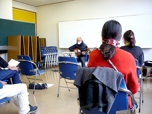 一人でギターを弾く50代男性の生徒さんとそれを聴く生徒さんたち