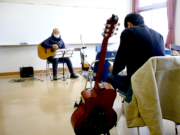 一人でギターを弾く生徒さん（50代男性）とそれを聴く生徒さんの様子