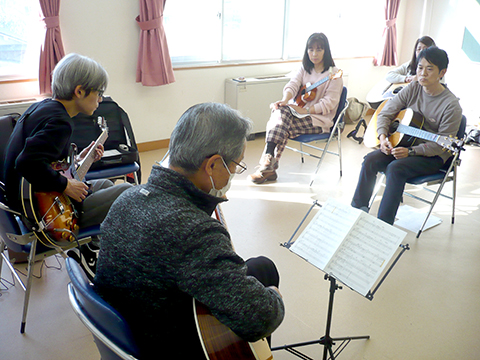 70代男性の生徒さんと講師のギター演奏とそれを聴く生徒さんたちの様子