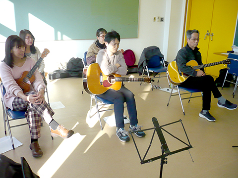 アコースティックギターを弾き語りする男性と演奏を聴く生徒さんの様子