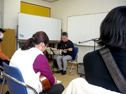 エレキギターを弾く40代男性と演奏を聴く生徒さんの様子
