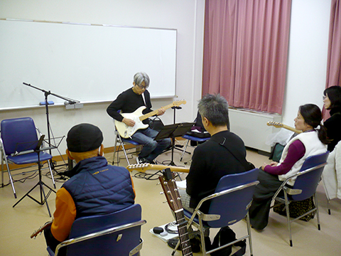 エレキギターを弾くギター講師と演奏を聴く生徒さんたちの様子