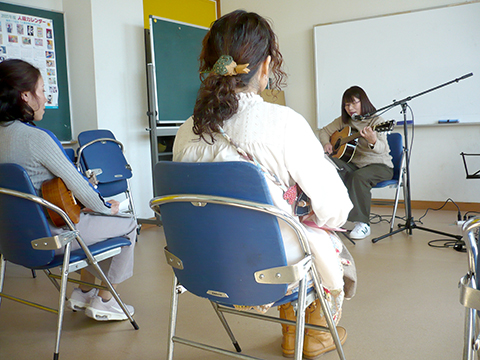 アコースティックギターを弾き語りする生徒さん(50代女性)とそれを聴く生徒さんの様子
