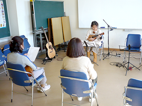 ウクレレを弾く50代女性とそれを聴く生徒さんたちの様子